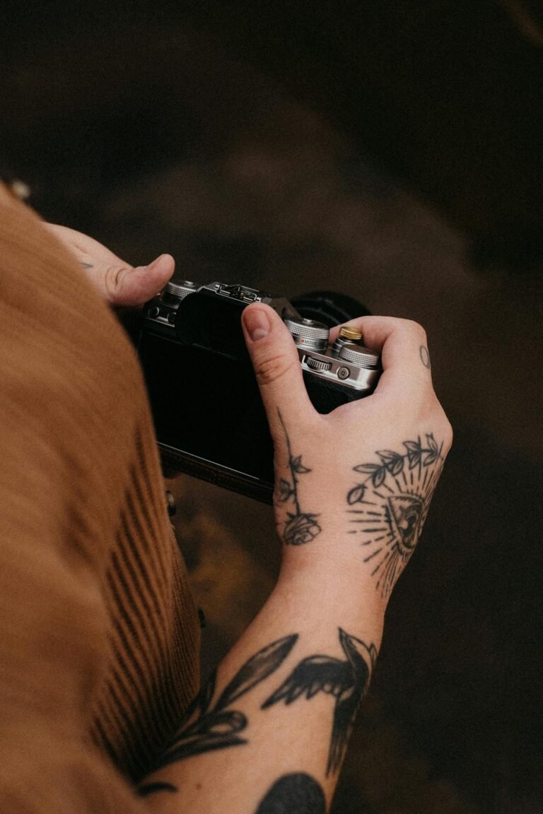 Close-up of tattooed hands holding a vintage camera, emphasizing artistic detail.